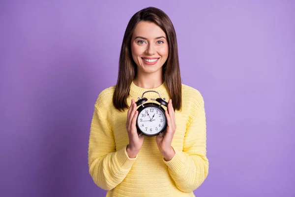 Çekici bir kadının iki elinde siyah bir saat tutarken çekilmiş fotoğrafı. Canlı mor renkli arka planda izole edilmiş bir şekilde gülümsüyor. — Stok fotoğraf