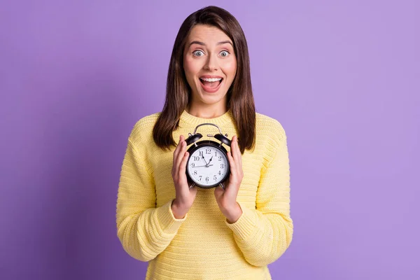 Photo portrait of excited girl holding black alarm clock in two hands with open mouth isolated on vivid purple colored background — Stock Photo, Image