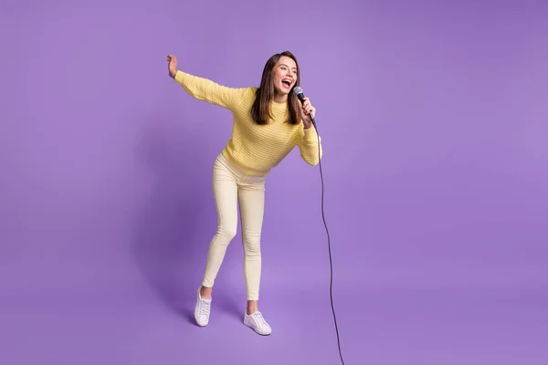 Foto de cuerpo entero de chica morena usando suéter amarillo sosteniendo micrófono cantando canción sonriendo aislado sobre fondo de color púrpura brillante —  Fotos de Stock