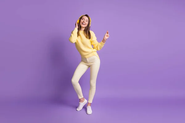 Foto de cuerpo entero de una morena soñadora escuchando música con auriculares amarillos modernos bailando aislados sobre un vibrante fondo de color violeta — Foto de Stock