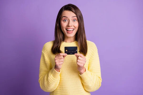 Foto de retrato de una chica alegre que sigue mostrando una tarjeta de crédito de plástico con atuendo amarillo casual sonriendo aislada sobre un fondo de color púrpura brillante — Foto de Stock