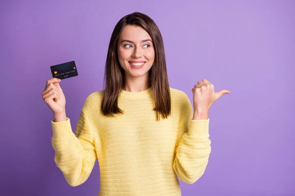 Фотопортрет красивої дівчини, що тримає банківську пластикову картку, показуючи на порожньому просторі посміхаючись, дивлячись на сторону ізольовано на яскраво-фіолетовому кольоровому фоні — стокове фото