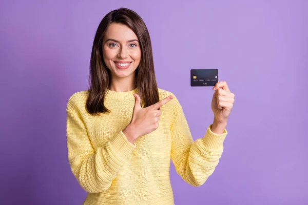 Foto porträtt av vacker flicka bär gul tröja pekar på kreditkort med finger leende isolerad på ljusa lila färg bakgrund — Stockfoto