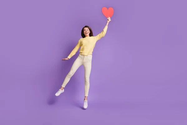 Foto retrato vista de cuerpo completo de chica emocionada sosteniendo tarjeta de corazón rojo grande saltando aislado sobre fondo de color violeta vivo —  Fotos de Stock