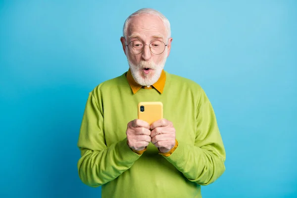 Emeklinin fotoğrafı, büyükbaba. Heyecanlı bir ağız. Akıllı telefon gözlüğü, yeşil süveter, mavi arka plan. — Stok fotoğraf