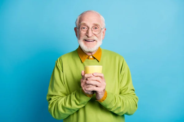 Foto de aposentado velho homem segurar copo olhar câmera alegre sorriso desgaste óculos verde suéter isolado azul cor fundo — Fotografia de Stock