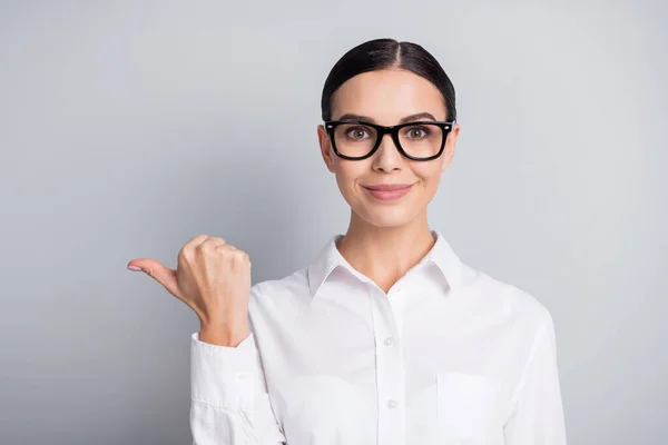 Foto de positivo adorável jovem senhora direto polegar vazio espaço desgaste branco camisa isolado cinza cor fundo — Fotografia de Stock