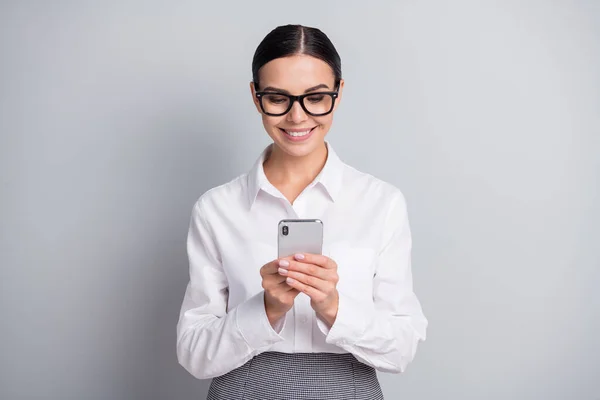 Φωτογραφία από χαρούμενα γυναίκα των επιχειρήσεων κατέχουν κινητό τηλέφωνο toothy χαμόγελο φορούν γυαλιά λευκό πουκάμισο απομονωμένο γκρι χρώμα φόντο — Φωτογραφία Αρχείου