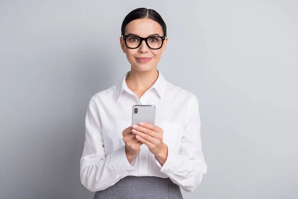 Foto de trabalhador positivo menina segurar telefone olhar câmera desgaste óculos branco camisa isolado cinza cor fundo — Fotografia de Stock