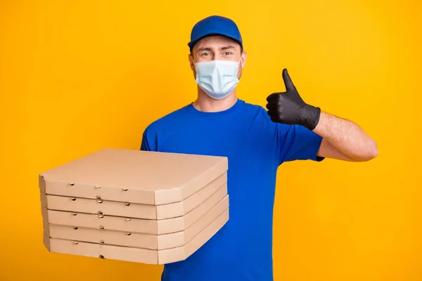 Foto de trabalho cara headwear segurar caixas de pizza mostrar polegar para cima segurança respiratória isolada no fundo de cor amarela — Fotografia de Stock