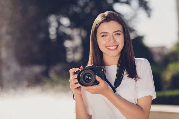 Foto retrato de una mujer sosteniendo una cámara digital con dos manos en el parque —  Fotos de Stock