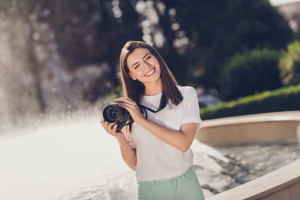 Foto retrato de niña sosteniendo cámara fotográfica digital con fuente detrás al aire libre —  Fotos de Stock