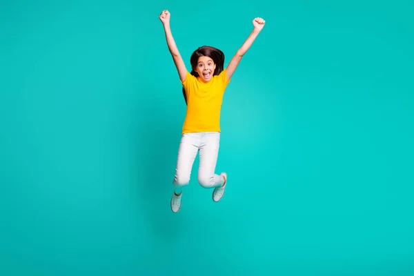 Foto de longitud completa de la chica extática salto levantar los puños usar camiseta amarilla pantalones blancos pantalones aislados sobre fondo de color turquesa —  Fotos de Stock