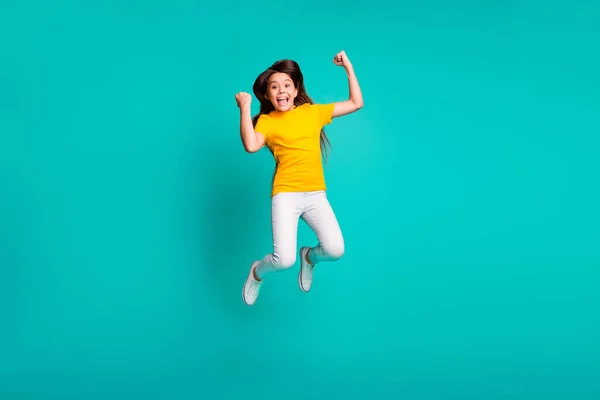 Full body foto van blij kind meisje springen hoog raise vuisten dragen witte broek geel t-shirt geïsoleerd over teal kleur achtergrond — Stockfoto