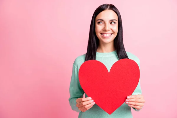Foto retrato de namorada curiosa mostrando papel vermelho coração cartão postal sorrindo olhando espaço vazio isolado no fundo cor-de-rosa pastel — Fotografia de Stock