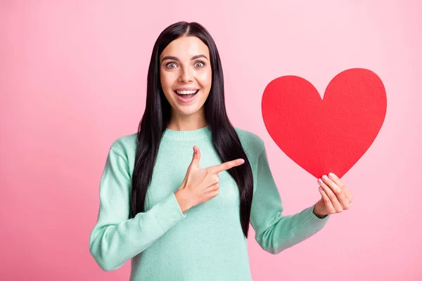 Foto retrato de mulher excitada apontando dedo grande no cartão de coração vermelho em uma mão isolada no fundo de cor rosa pastel — Fotografia de Stock