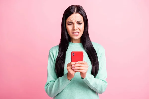 Foto retrato de una mujer asustada mordiendo el labio inferior sosteniendo el teléfono con dos manos aisladas sobre fondo de color rosa pastel — Foto de Stock