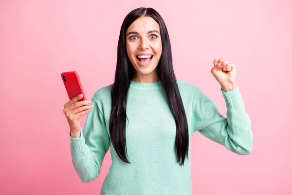 Foto retrato de menina celebrando animado com o punho levantado segurando telefone em uma mão isolada no fundo de cor rosa pastel — Fotografia de Stock