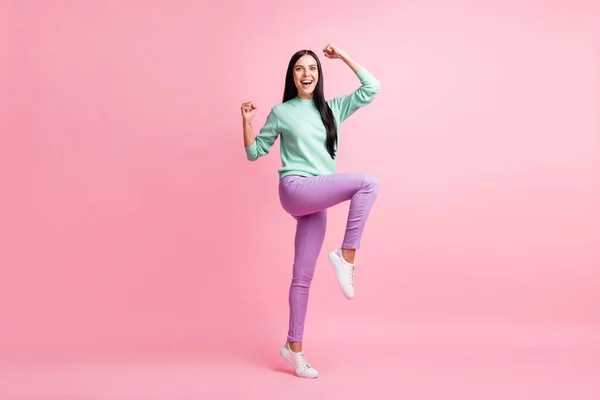 Foto de longitud completa de adorable afortunada joven dama usar jersey de color verde azulado levantamiento brazos manos puños de pie una pierna aislado color rosa fondo —  Fotos de Stock