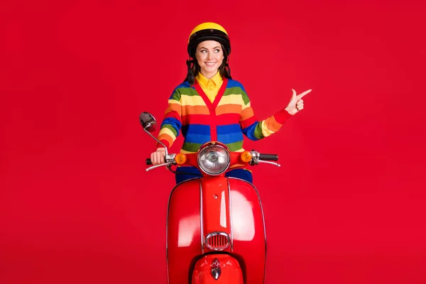 Foto porträtt av kvinna pekar finger ser till sidan körning scooter isolerad på levande röd färgad bakgrund — Stockfoto