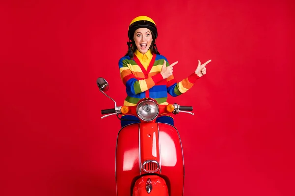 Foto portret van opgewonden schreeuwende vrouw wijzen twee vingers naar kant rijden retro scooter geïsoleerd op levendige rood gekleurde achtergrond — Stockfoto