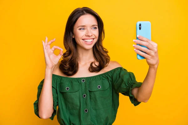 Zdjęcie wesoły brunetka kręcone włosy pani trzymać telefon zrobić selfie pokazać okay znak izolowane na żółtym tle kolor — Zdjęcie stockowe