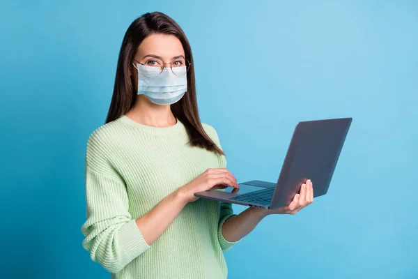 Φωτογραφία του θετικού κοριτσιού που εργάζεται σε φορητό υπολογιστή φορούν μπλε μάσκα προσώπου απομονώνονται σε μπλε φόντο χρώμα — Φωτογραφία Αρχείου