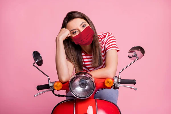 Porträt eines Mädchens auf einem Moped sitzend mit roter Gesichtsmaske isoliert über rosa Pastellfarbe Hintergrund — Stockfoto