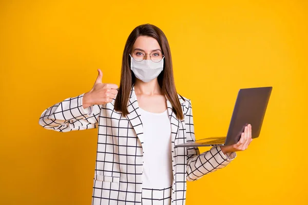 Foto portret van de vrouw die werkt op laptop met duim-up dragen van witte masker geïsoleerd op levendige gele kleur achtergrond — Stockfoto