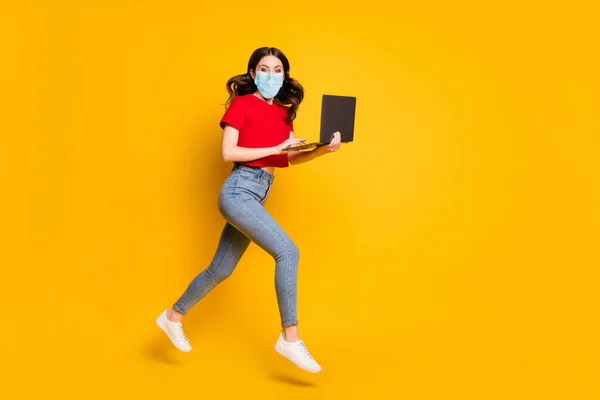 Full längd profil sida foto av flicka arbete bärbar dator internet försäljning hoppa springa bära mask t-shirt denim isolerad gul färg bakgrund — Stockfoto