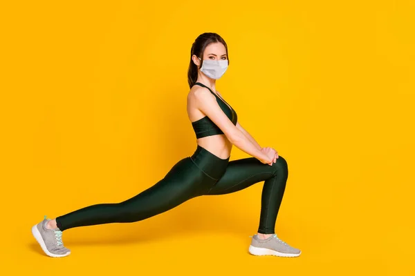 Photo de sport jeune dame étirement assis une jambe porter masque sport costume haut pantalon baskets isolé couleur jaune fond — Photo