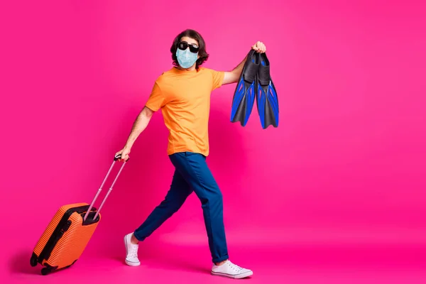 Volledige lengte profiel foto van man lopen ruim bagage flips covid grenzen sluiten dragen medisch masker geïsoleerde roze kleur achtergrond — Stockfoto