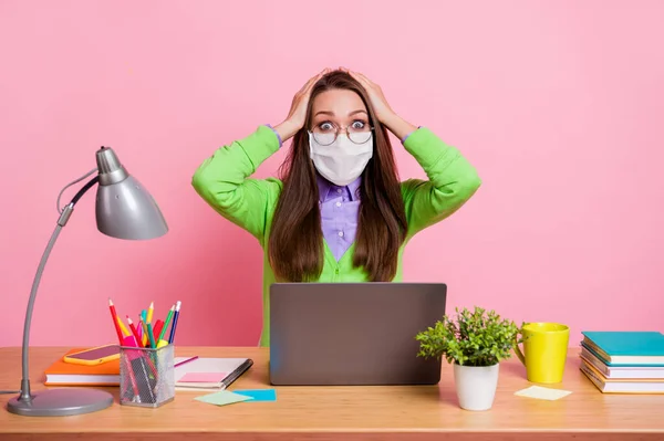 Foto van verbaasd werknemer meisje aanraken handen hoofd slijtage shirt medisch masker zitten tafel geïsoleerde pastel kleur achtergrond — Stockfoto