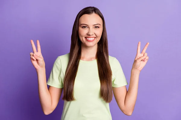 Portrait of funny young woman show two hands fingers v-sign light green clothing isolated on purple color background — 图库照片