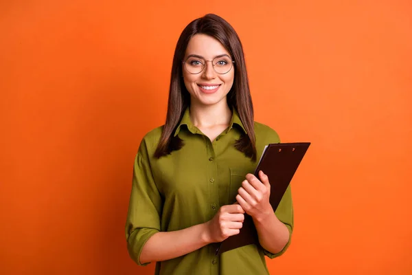 Foto-Porträt einer Arbeiterin mit Klemmbrett lächelnd trägt Brille grünes Hemd isoliert auf lebendigen orangefarbenen Hintergrund — Stockfoto