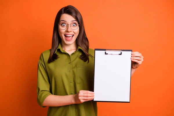 Foto retrato de chica impactada demostrando portapapeles espacio vacío mirando la boca abierta aislada sobre fondo de color naranja brillante — Foto de Stock