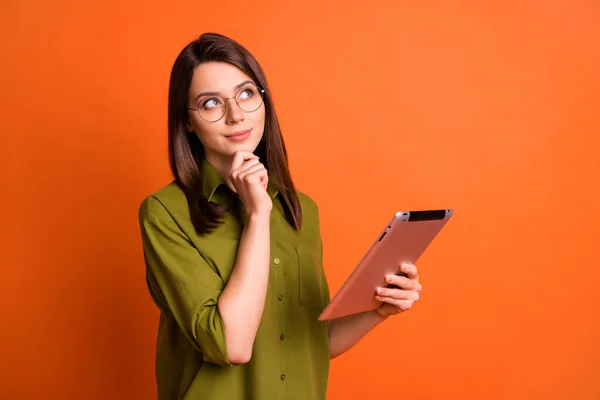 Foto portrét snivé brunetky student přemýšlet o myšlence udržet tablet izolované na jasně oranžové pozadí — Stock fotografie