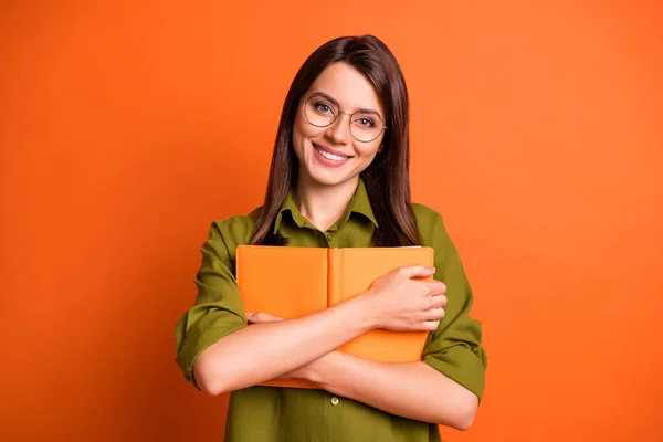 Foto ritratto di carina bella ragazza bruna tenendo abbracciare libro sorridente isolato su vibrante sfondo di colore arancione — Foto Stock