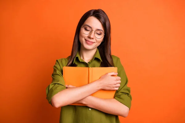 Foto retrato de bonito sonhador morena menina segurando abraçando livro fechado olhos isolados no fundo de cor laranja brilhante — Fotografia de Stock