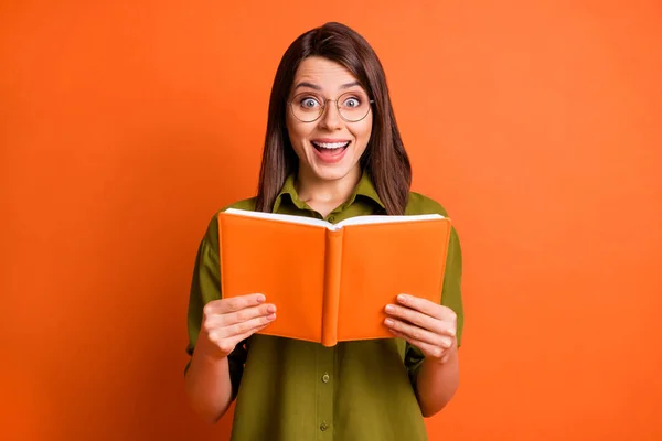 Foto retrato de chica morena sorprendida manteniendo libro riendo aislado sobre fondo de color naranja vivo — Foto de Stock