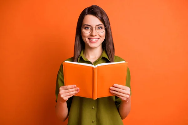 Foto ritratto di studentessa allegra indossando occhiali mantenendo libro sorridente isolato su vibrante sfondo di colore arancione — Foto Stock