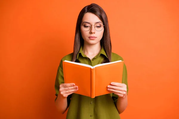 Foto portret van geconcentreerde vrouwelijke student dragen bril lezen boek geïsoleerd op fel oranje kleur achtergrond — Stockfoto