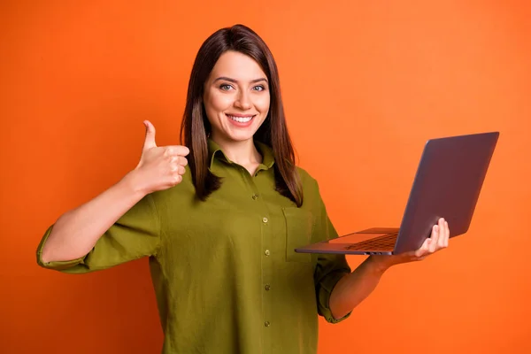 Canlı turuncu arka planda izole edilmiş, gülümseyen bir jest gösteren bilgisayar kullanan genç bir kadın ressamın fotoğrafı. — Stok fotoğraf