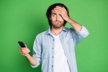 Portrait of his he nice attractive unsure depressed clueless guy using device browsing post news face palm dont know isolated over bright vivid shine vibrant green color background clipart