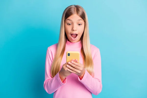 Photo portrait of amazed schoolgirl with opened mouth using cellphone staring reading information isolated on bright teal color background — Stock Photo, Image