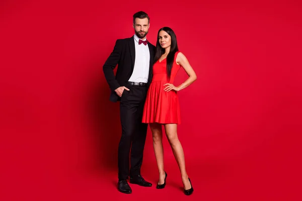 Фотографія оптимістичної пари стоїть у яскравій сукні чорний костюм ізольований на червоному тлі — стокове фото
