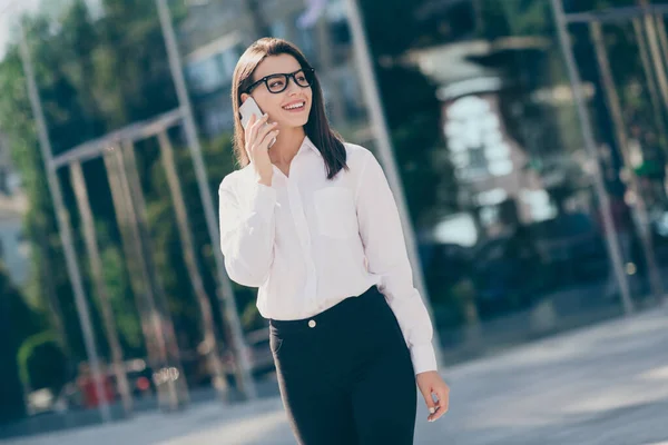 Foto de mujer joven adorable confiado usar gafas de camisa formal blanco hablando dispositivo moderno mirando al aire libre — Foto de Stock