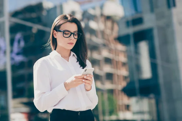 Foto de dulce mujer joven seria usar gafas de camisa formal blanca sosteniendo buscando dispositivo moderno al aire libre — Foto de Stock