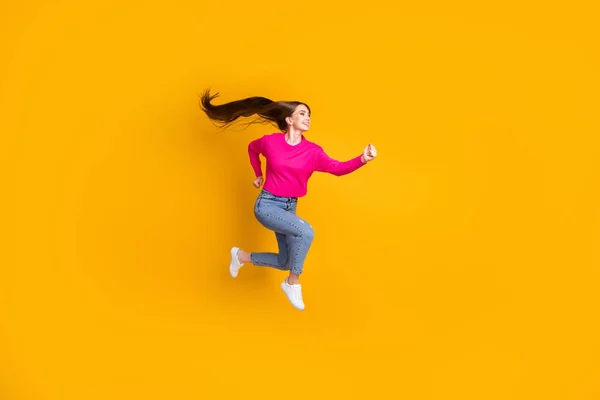 Foto de perfil de longitud completa de encantadora dama salto aire largo peinado desgaste rosa jersey jeans zapatillas aisladas de color amarillo fondo —  Fotos de Stock