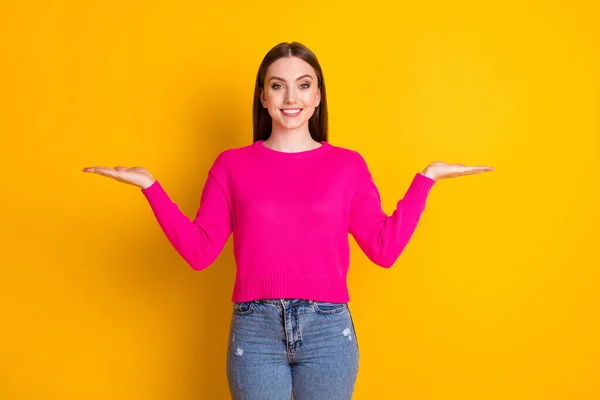 Foto de chica bonita sostener dos manos espacio vacío radiante sonrisa usar suéter rosa aislado color amarillo fondo —  Fotos de Stock